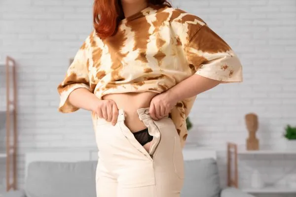 Image of woman trying to do her trousers up after pregnancy weight gain Barry